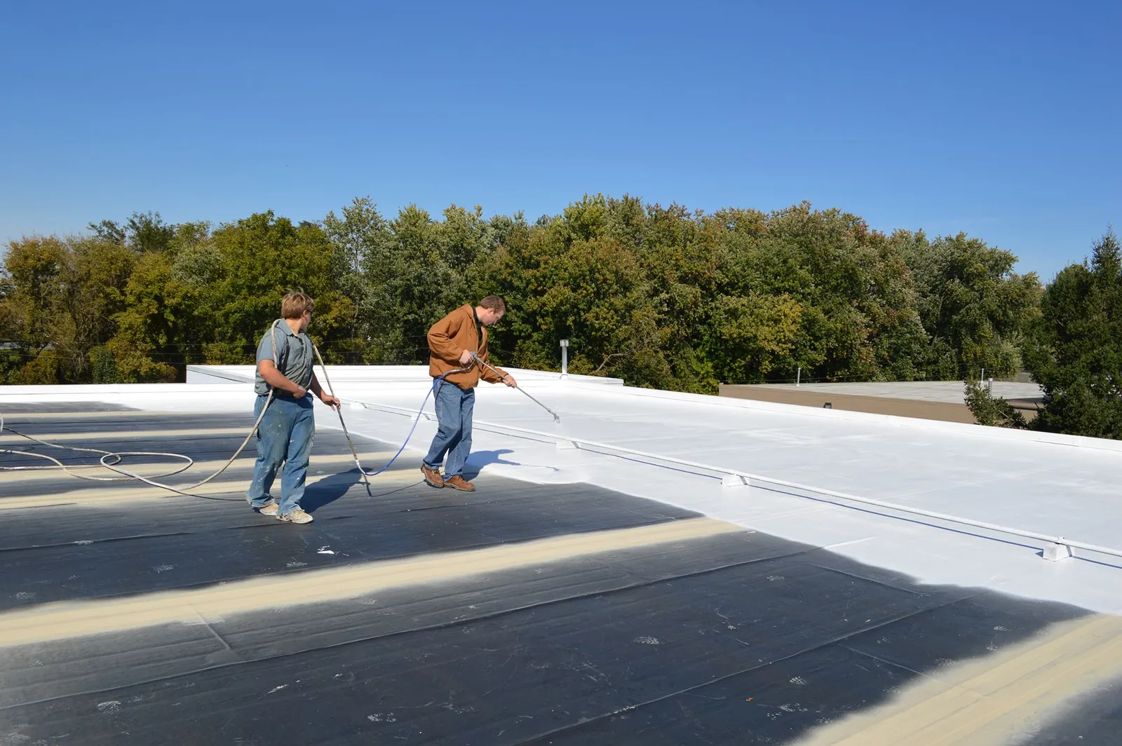 Roofers rolling a white elastomeric coating onto a flat commercial roof