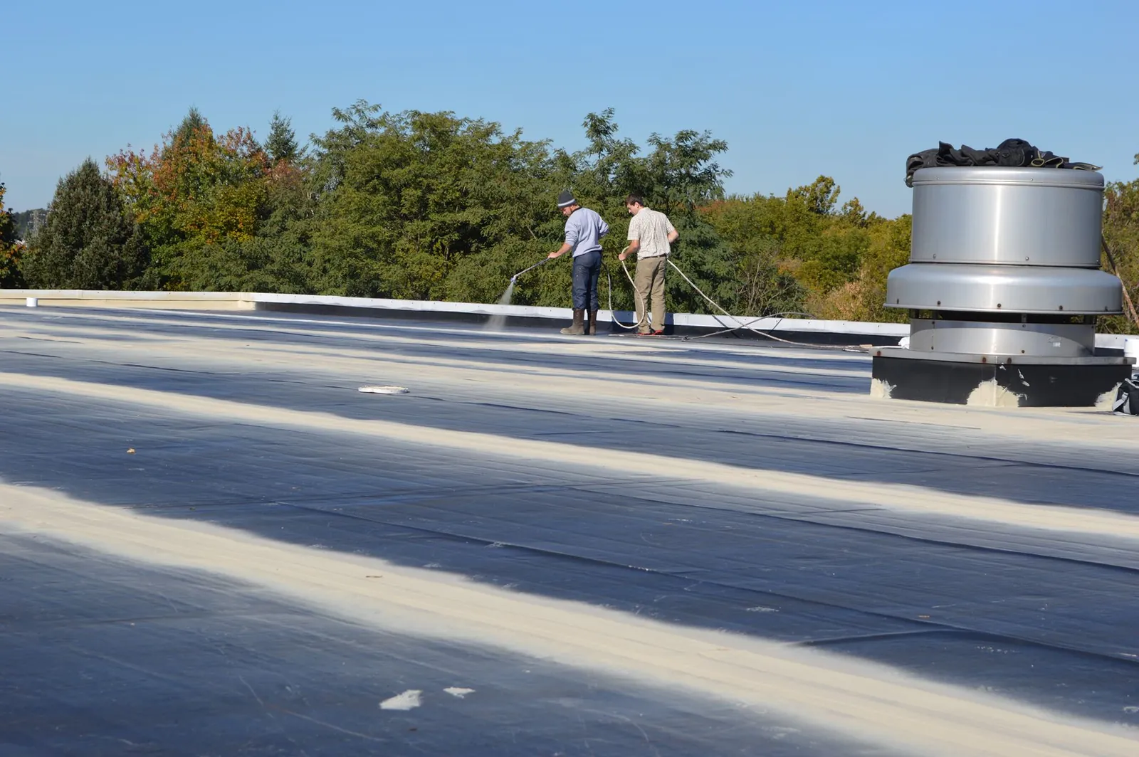 Two roofers power washing a flat membrane roof before a coating system