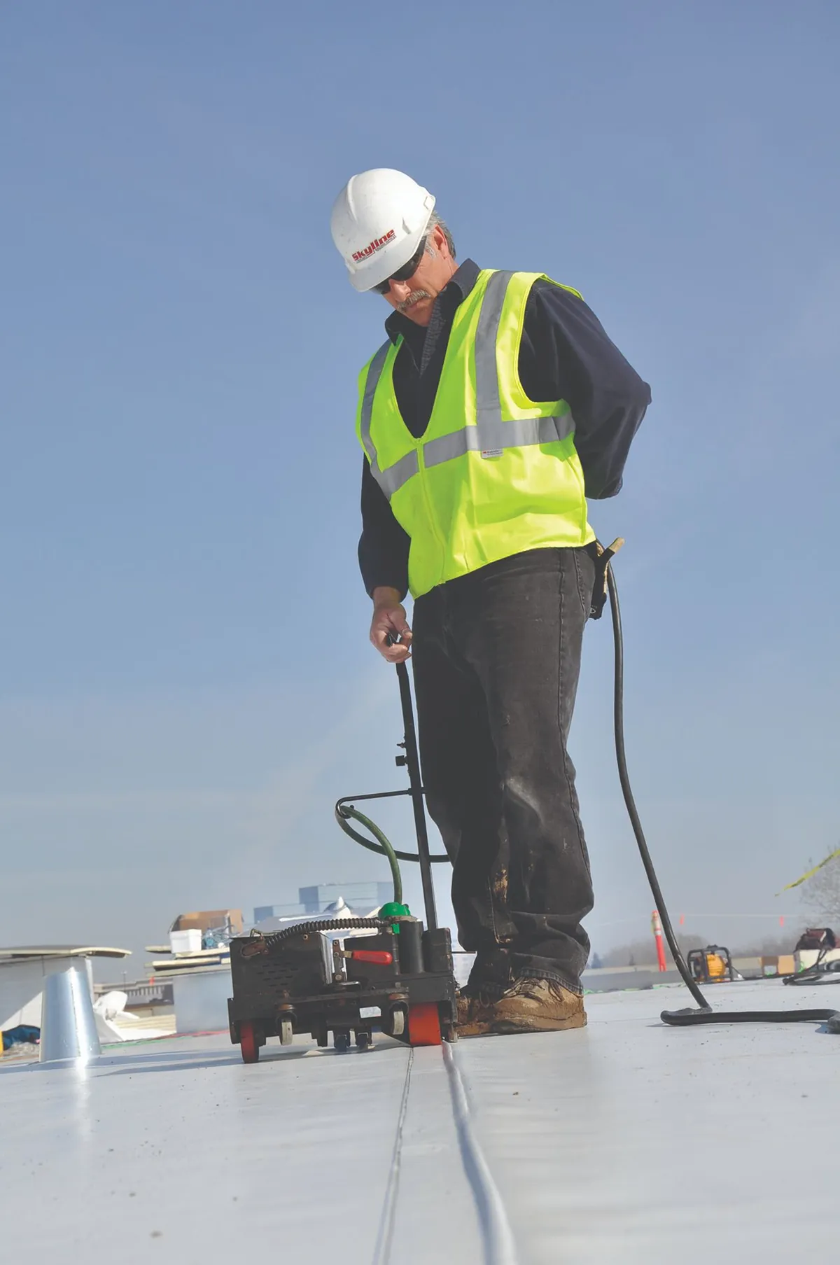 Roofer heat welding a single-ply membrane seam with a robotic welder