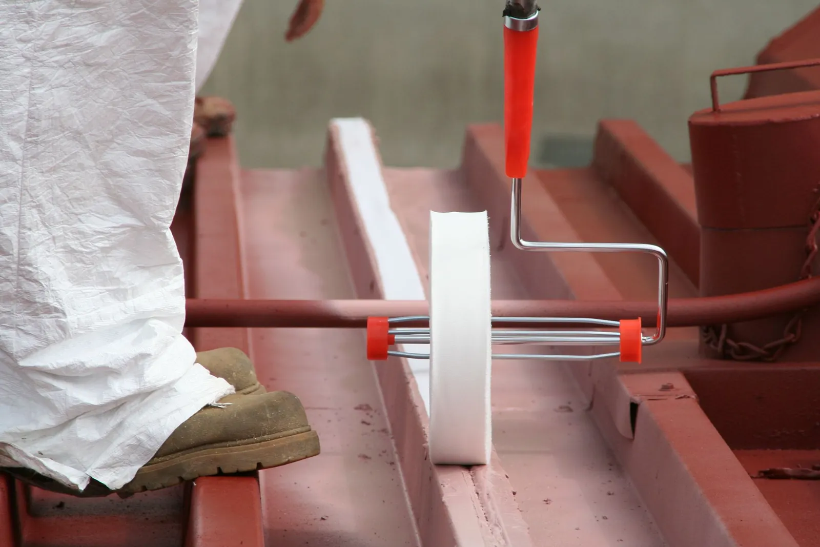 Roller applying coating over a reinforced seam on a red metal roof