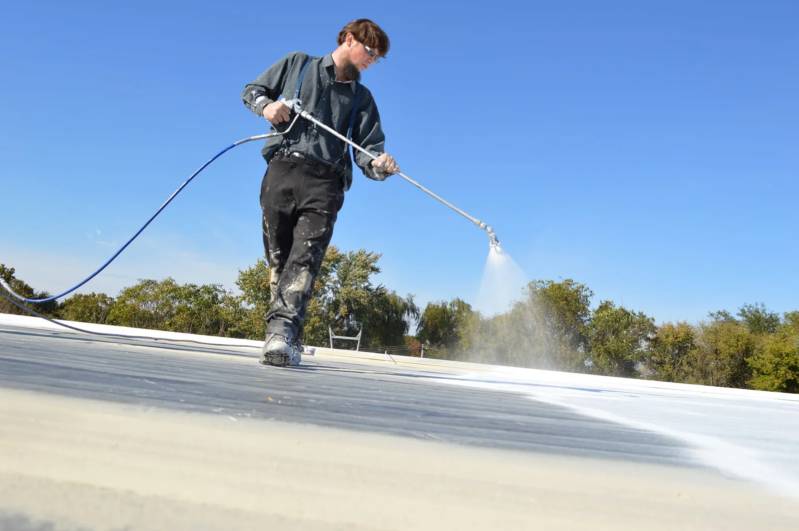 Roofer power washing a membrane roof to prepare it for coating
